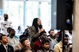 Eine Teilnehmerin des African Students Day 2026 steht im Publikum, hält ein Mikrofon und stellt eine Frage, während andere aufmerksam zuhören.